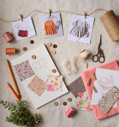 A mood board of garment sketches, fabric swatches, and buttons pinned to string.