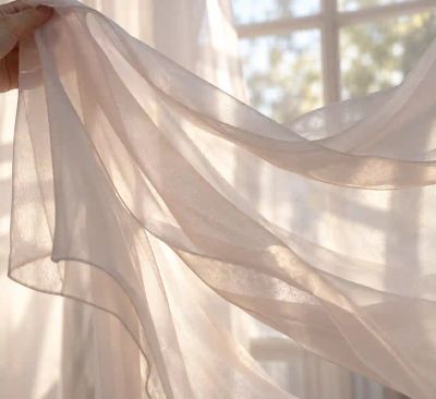 A length of sheer silk chiffon lifted by hand, light passing through it to show its sheerness and movement.