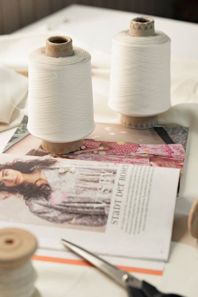 Thread cones resting on a pattern magazine next to a pair of scissors.