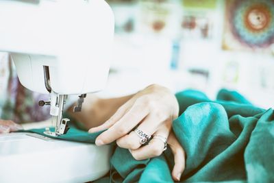 A hand guiding teal fabric under a sewing machine needle.