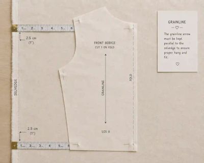A bodice pattern piece pinned to fabric with its grainline arrow measured parallel to the selvedge.