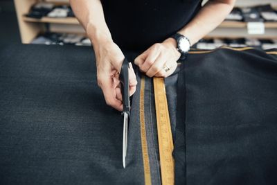 Hands cutting dark fabric along a tape measure with sewing shears.