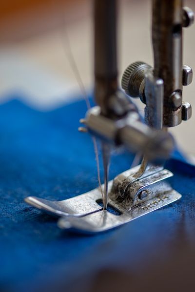 A sewing machine needle stitching into blue fabric, close up.