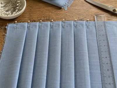 A row of crisp, pressed pleats pinned in place, a ruler alongside showing even spacing between folds.