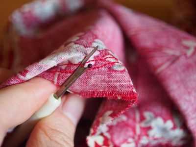 A hand pinning and hand-sewing along the edge of red floral fabric.