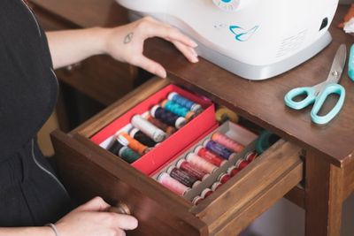 A hand opening a drawer of organized thread spools next to a sewing machine.