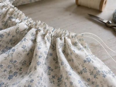 Blue fabric mid-gather along a drawn-up thread, the stitching line and bunched fullness visible.