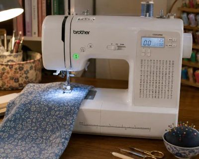 A home sewing machine threaded and stitching floral fabric on a work table.