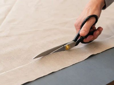 Shears mid-cut through a single layer of fabric, blades open along a marked cutting line.