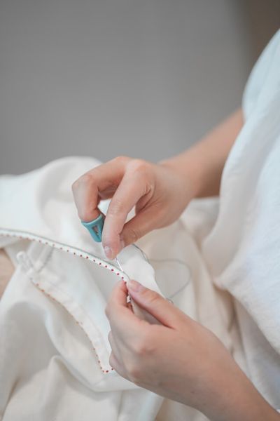 A hand finishing a fabric edge by hand with a needle and thread.