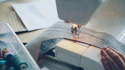 A sewing machine stitching a seam into gray fabric marked with construction lines.
